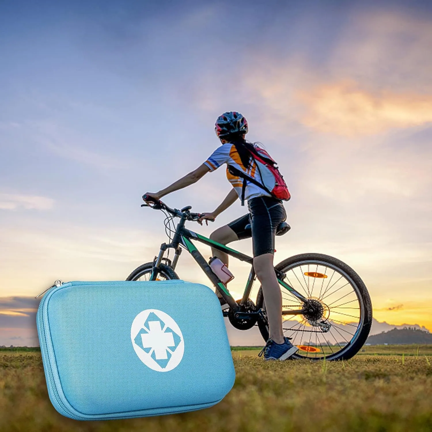 A blue AMORNING first aid kit in a field as a cyclist rides a hill at sunset