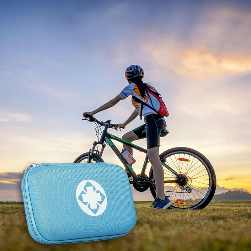 A blue AMORNING first aid kit in a field as a cyclist rides a hill at sunset