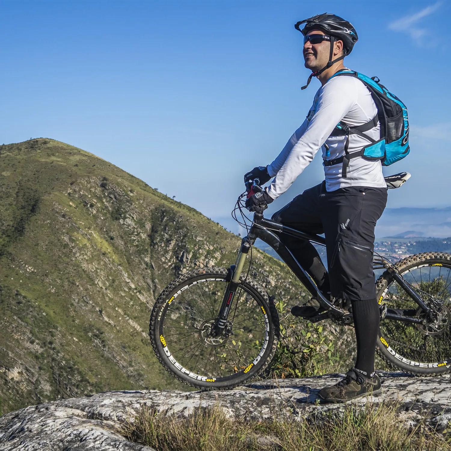 A mountain biker with a hydration pack stops on a rocky hilltop