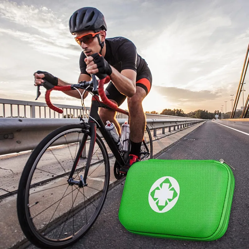 A green AMORNING first aid kit on the road shoulder as a road cyclist rides past