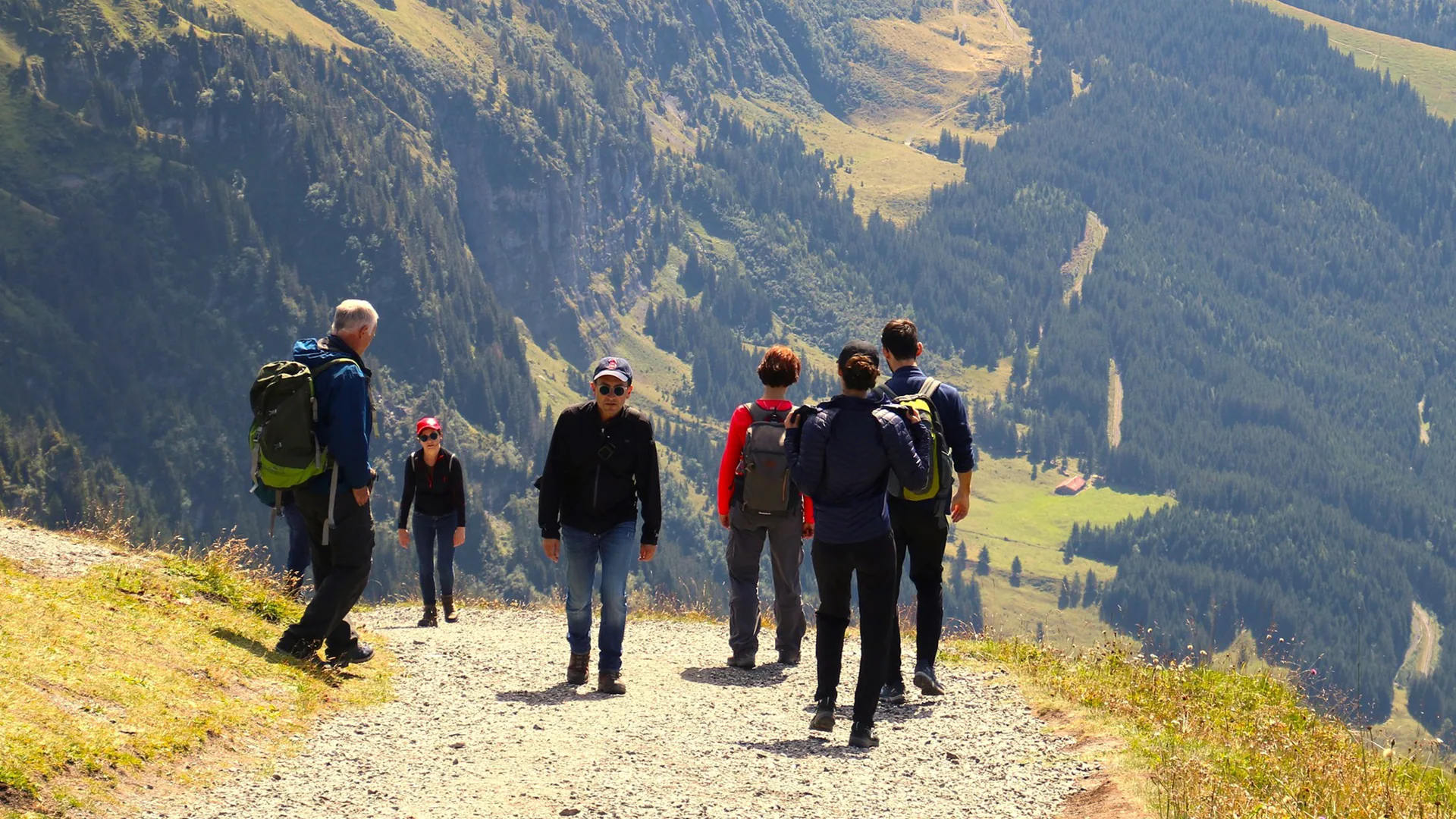 A group of hikers on a gravel trail above a green mountain valley