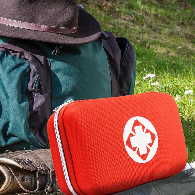 A red AMORNING first aid kit on the grass beside a felt hat and hiking boots