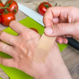 A plaster going onto a hand at a kitchen cutting board