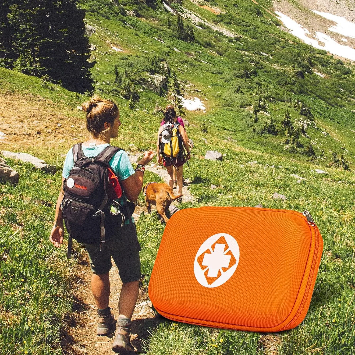 An orange AMORNING first aid kit on a mountain trail as two hikers and a dog walk up