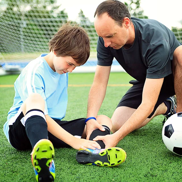 An adult checks a young player's knee on a soccer field